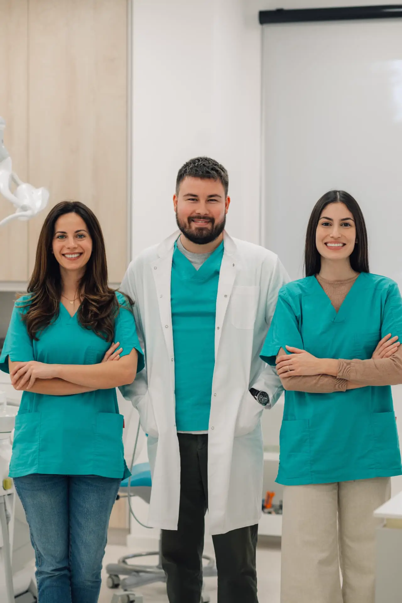 Three dental clinicians — two in teal scrubs and one in a white lab coat — standing together in a bright modern practice