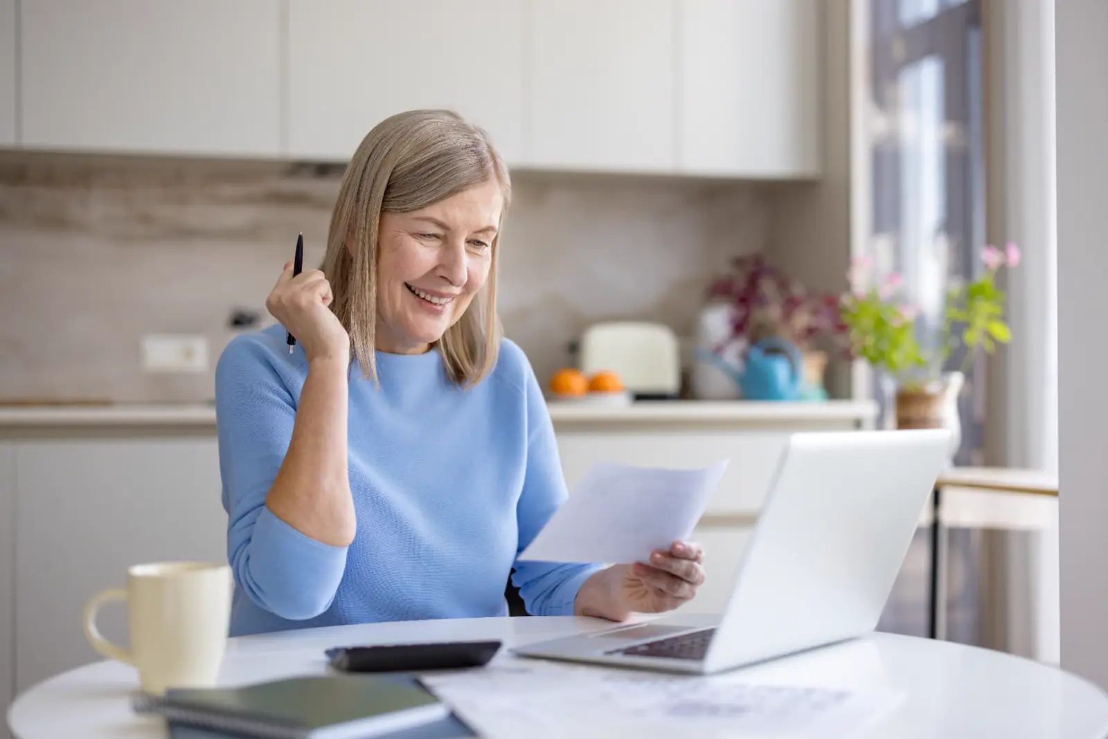 Smiling woman reviewing documents at a laptop with a calculator and coffee mug